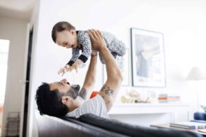Happy father lifting daughter while sitting on sofa at home